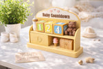 May include: A yellow baby countdown calendar with a bottle, blocks, and a teddy bear. The blocks show numbers 1, 2, and 4. A drawer has footprints. The words "Baby Countdown" are at the top.